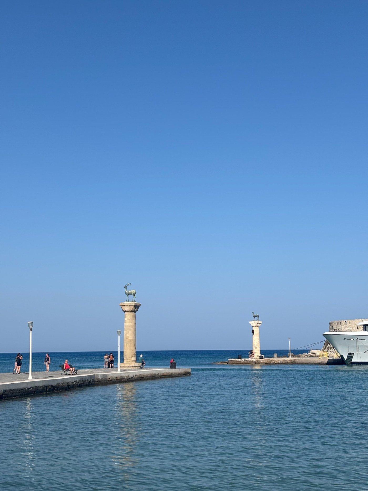Mandraki Harbour in Rhodes with stone columns topped by bronze deer statues, traditionally believed to mark the site of the Colossus of Rhodes.
