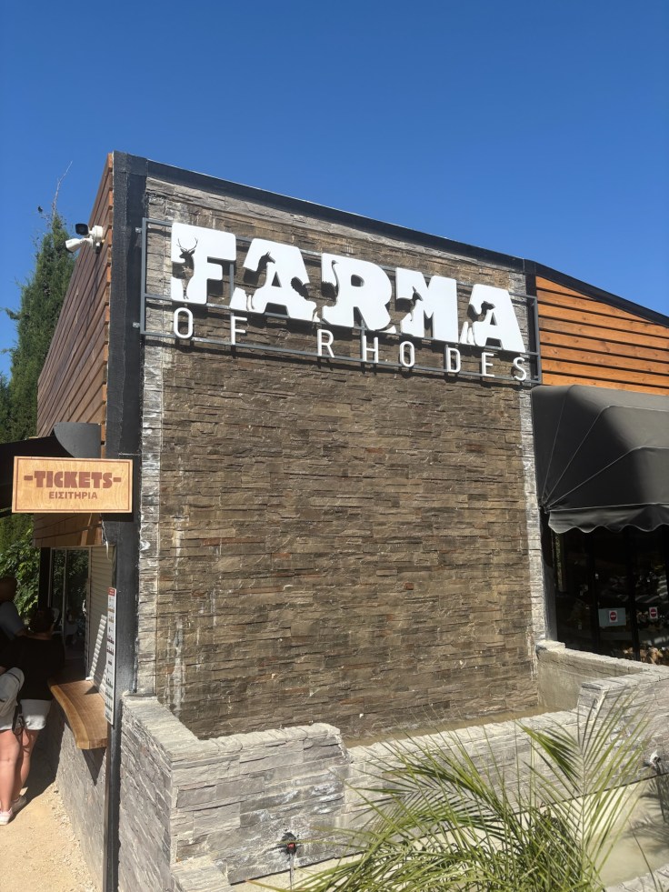 Entrance sign at Farma of Rhodes petting zoo on a sunny day.