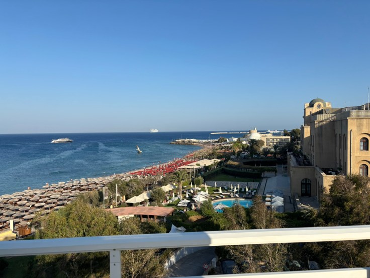 View of the Rhodes coastline and beach from the top‑floor terrace at Amalia Apartments.