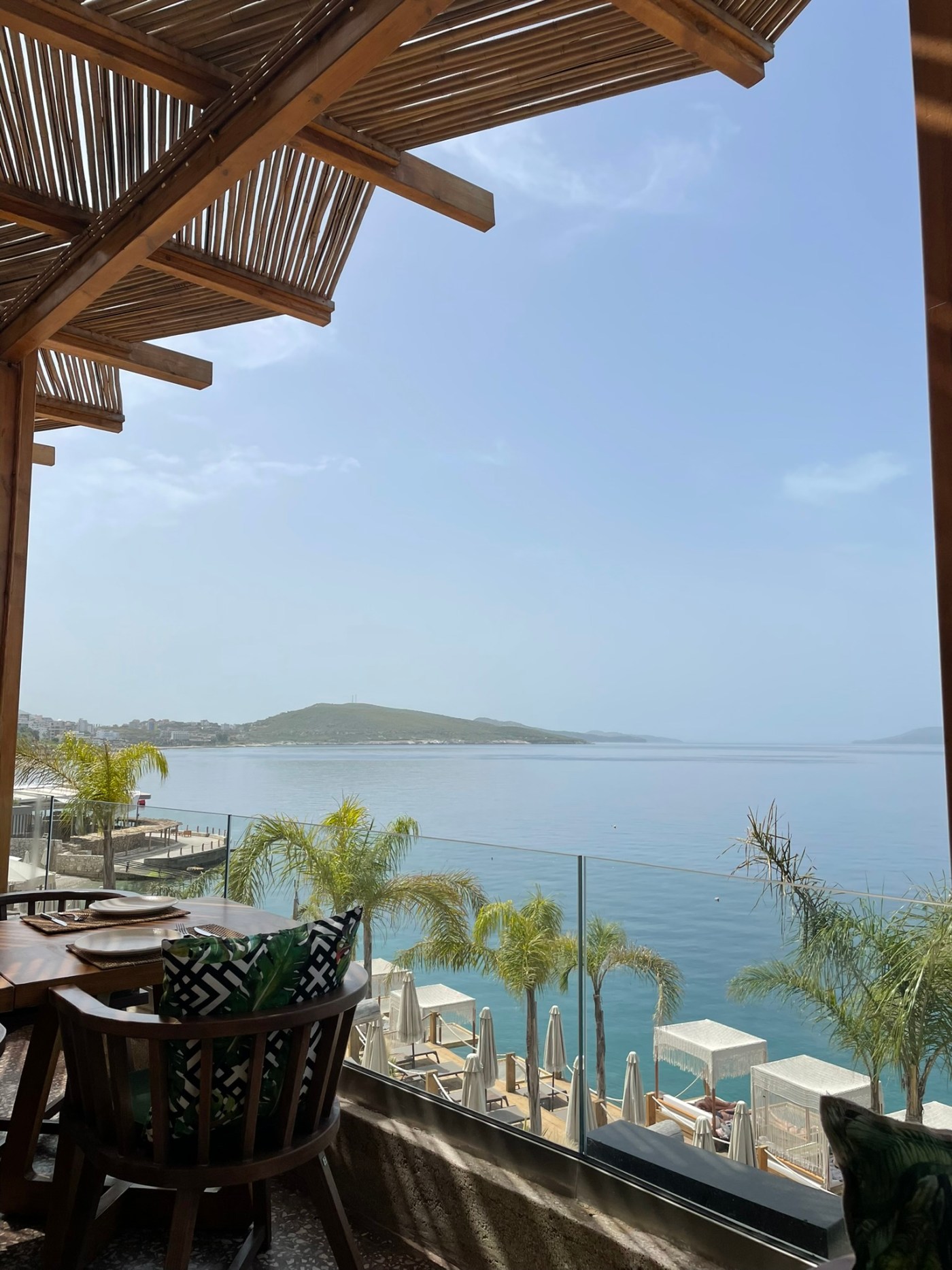 Shaded terrace overlooking palm trees, sun loungers, and the calm Ionian Sea at Lost Island Beach Club in Sarandë, Albania.