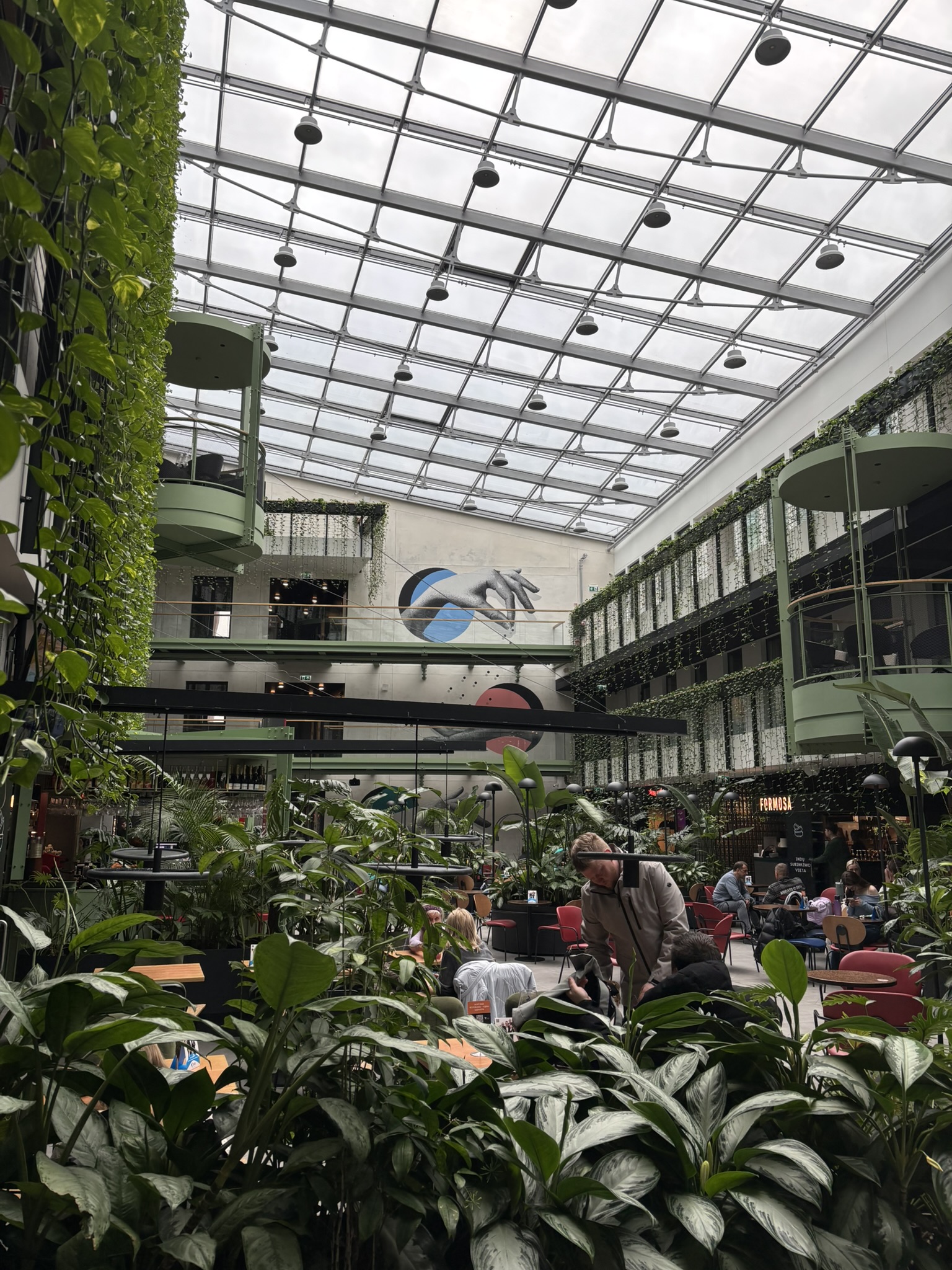 Indoor food hall with glass ceiling, greenery, and seating area in Vilnius
