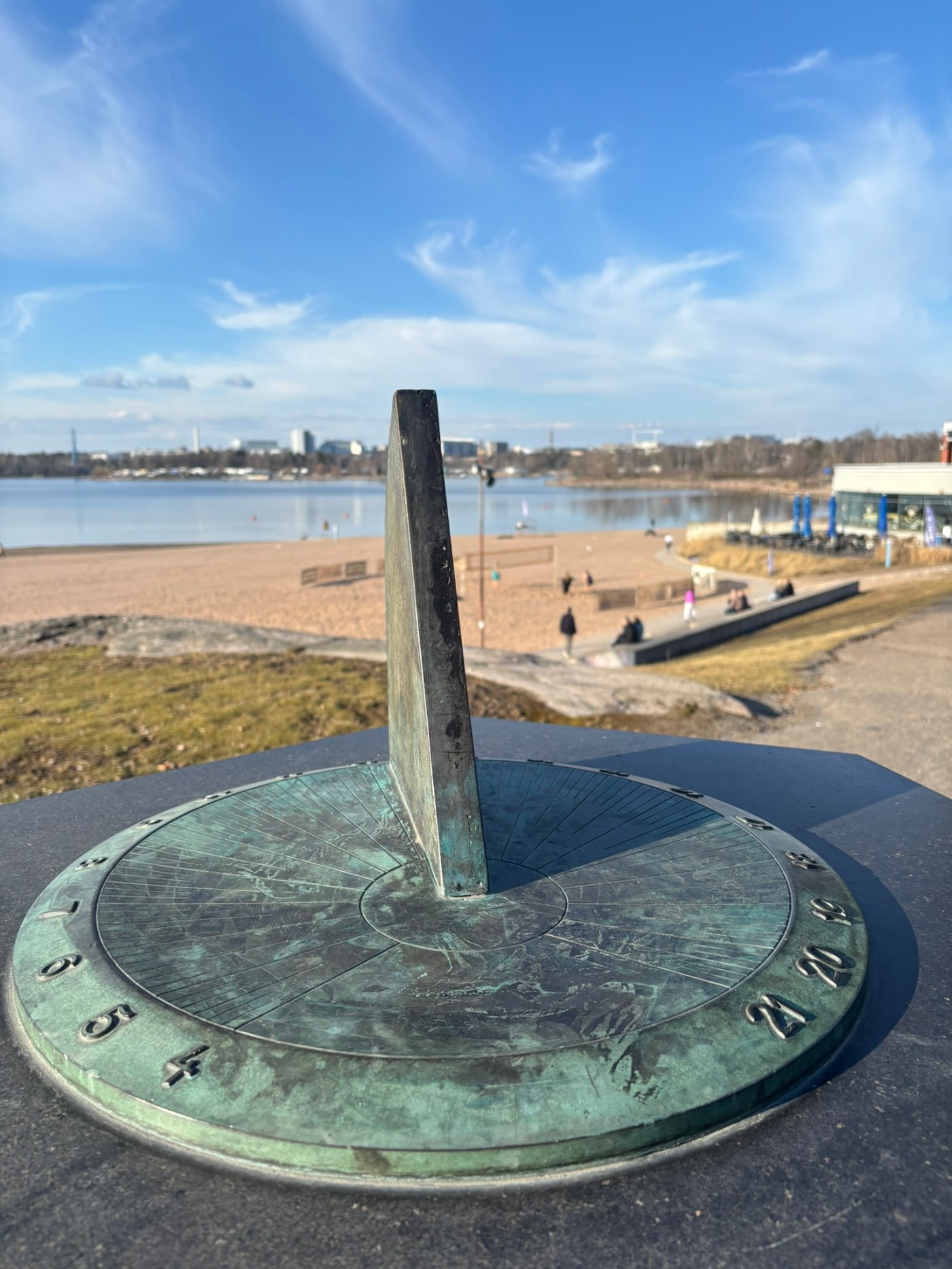 Sundial overlooking a sandy beach and calm waterfront in Helsinki, Finland under a clear blue sky